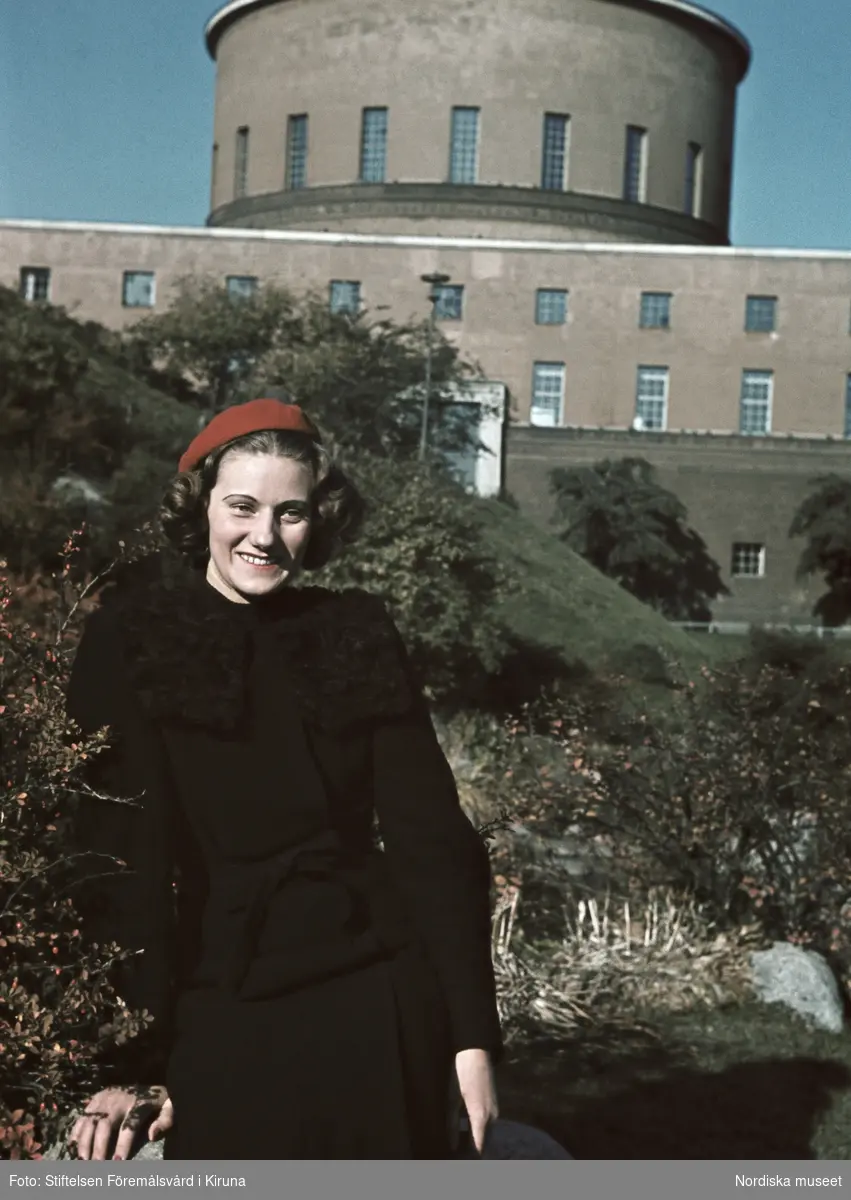 Kvinna iklädd svart dräkt och röd basker. Stockholms stadsbibiliotek i bakgrunden.