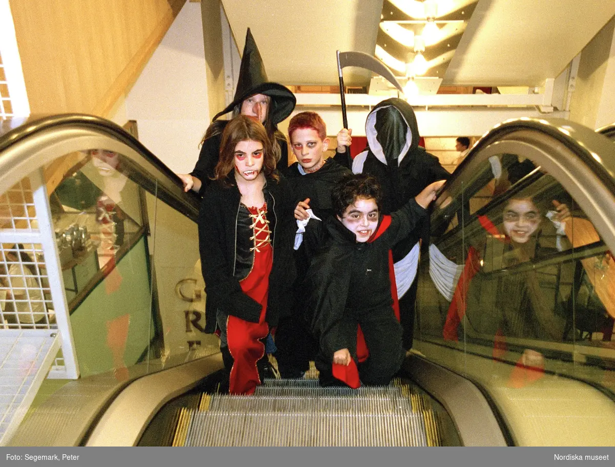 Utklädda barn i rulltrappa. Förberedelser och firande av Halloween.