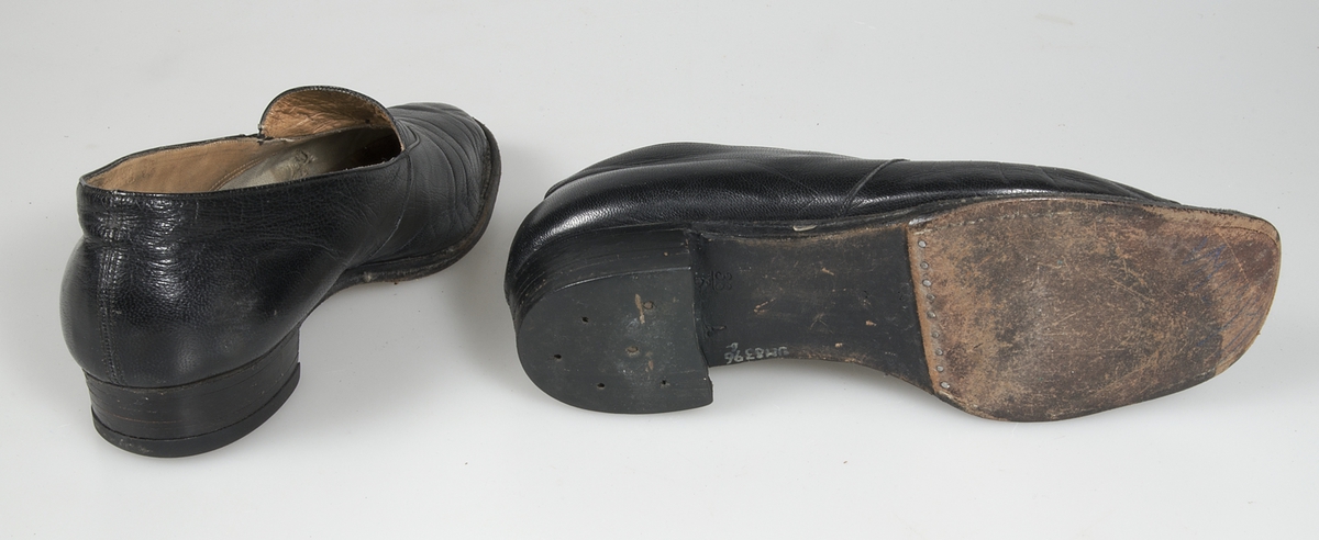 Ett par skor av svart skinn. Halvsulad lädersula. Fodrad med brunt skinn och lärft. Märkt: Marta-skor Oscaria-Örebro. Storlek 38.