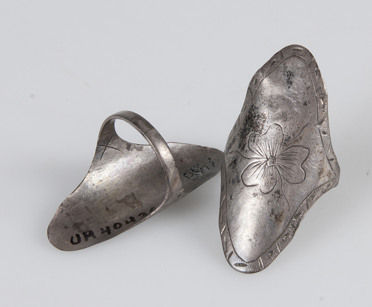 Två ringar av silver, med ovala plattor. Plattorna är graverade, en smal kantdekor och en blomma.  Märkta B.979. 