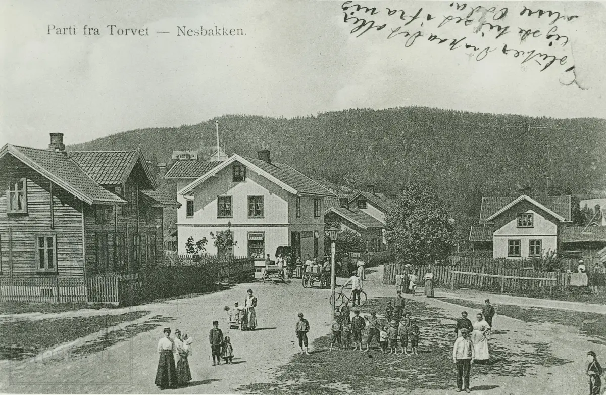 Parti fra torvet på Nesbakken med bygninger og personer oppstilt på torvet.