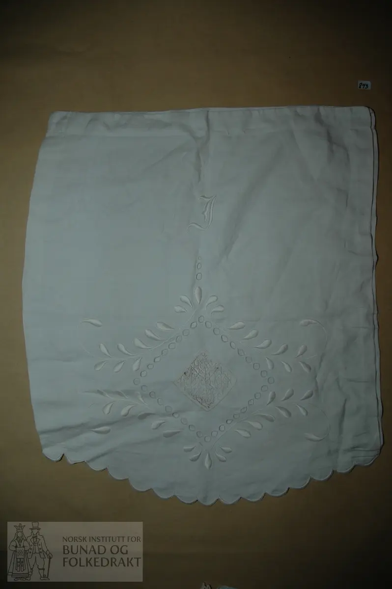 Pose til oppbevaring av klede i kvit bomullslerret pryda med engelsk broderi, innfelling av ein hekla firkant og initial. Fold i kvar side og løpegang øverst.