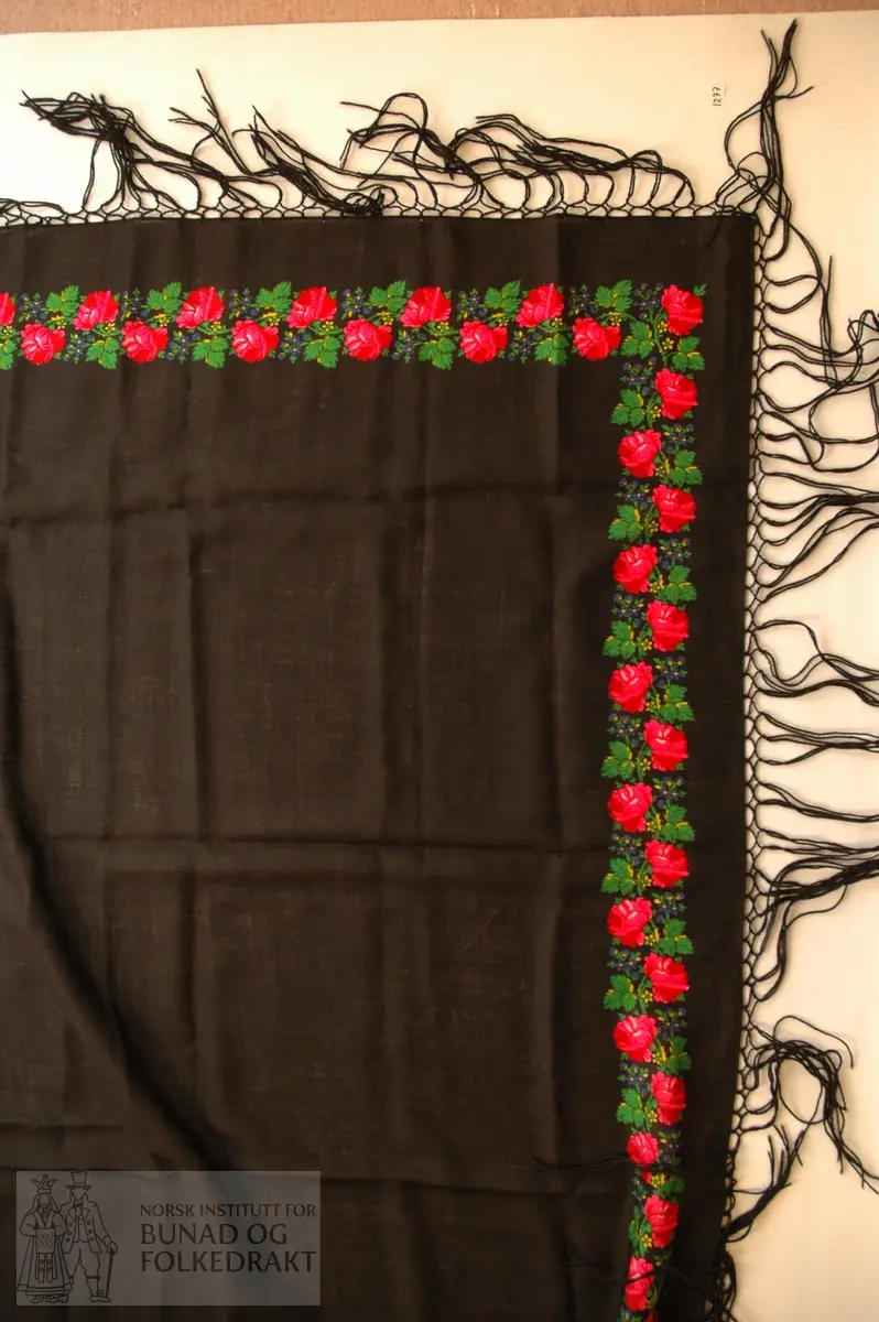 Sjal i svart ullmouseline med påknytta frynser, kypertvove. Trykt rosemønster i fleire fargar.