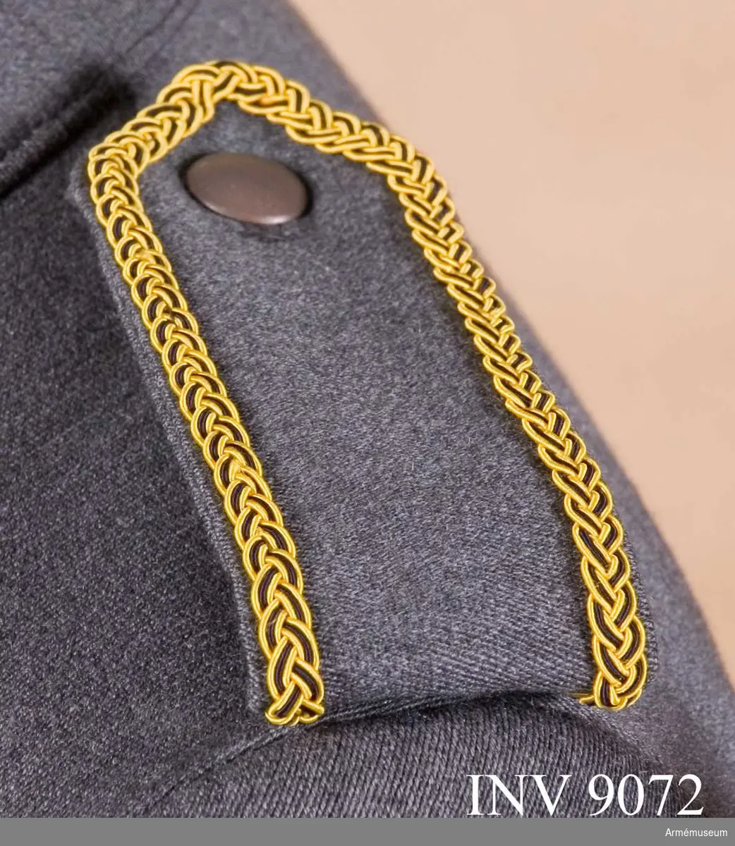 Av samma tyg och färg som jackan kantad med en flätad galon i gult och svart silke. Tecken för kårchef. Axelklaffen är dubbel och viks runt en träns vid axelsömnen och knäpps mot en grå knapp av mindre modellen på jackan.