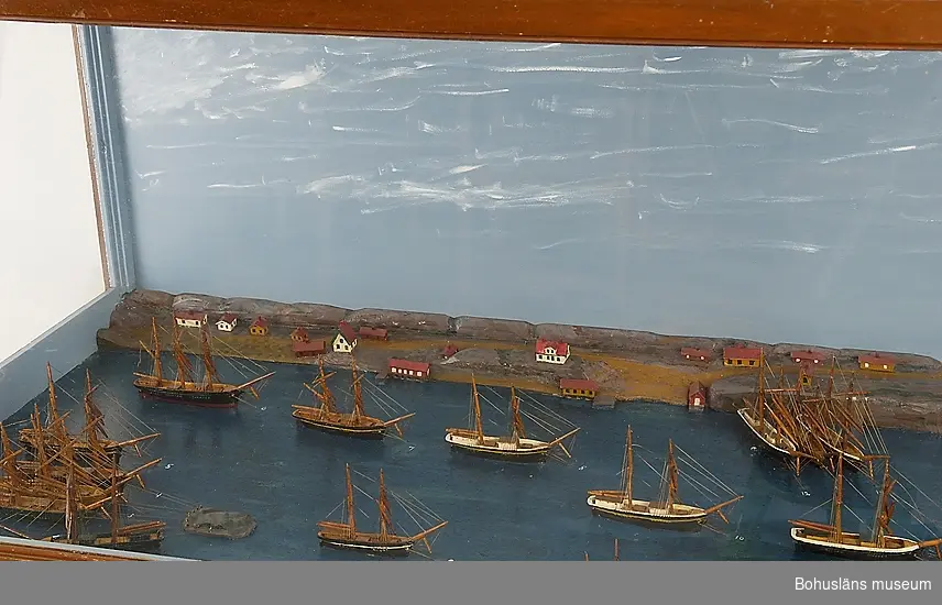 Panorama i monter över Fiskebäckskils hamn på 1880-talet med 33 fartygsmodeller i vinterkvarter.
Tillverkad av kapten John Emil Olsson (1880-1950), Fiskebäckskil på Skaftö i Lysekils kommun 1942.
Trä, metall, lintråd, gips, glas, målat med oljefärg.
Största fartygsmodell längd 16 cm; monter 202 x 61 cm, höjd 53 cm; okänd skala. Vattenlinjemodeller av 30 råseglare, två större jakter och en galeas, uppankrade eller förtöjda. Stående och löpande rigg, däckshus och lastluckor, målade och lackade placerade på en blåmålad platta. Bakgrund av utskurna och målade berg med ett 30-tal hus, sjöbodar och bryggor utspridda längs den djupgående kilen och med gatten ut mot Gullmaren.

Framtill på modellens långsida står textat med vita tryckbokstäver: 
FISKEBÄCKSKIL:S HAMN I SLUTET AV 1880-TALET.
VID VARJE FARTYGS FÖR STÅR EN SIFFRA SOM HÄNVISAR TILL TAVLAN OVANFÖR MONTERN.
Den maskinskrivna texten berättar:
Fiskebäckskils hamn i slutet av 1880-talet. 
I vinterkvarter upplagda i Fiskebäckskil hemmahörande segelfartyg.
1. Skonert Gustaf, befälhavare M. Johansson
2. Brigg Clinton, befälhavare J. Bengtsson
3. Skonertskepp Nordstjernan, befälhavare Am. Olsson
4. Barkskepp Diana, befälhavare H. Andersson, Gåsö
5. Skonert Elise, befälhavare Joh. Gren
6. Barkskepp Celeritas, befälhavare C. Bengtsson
7. Brigg Ben:s Mollén, befälhavare Joh. Månsson
8. Skonerter Elida, Magnus Gren
9. Skonert Olga, befälhavare C. Jansson
10. Skonert Idun, befälhavare Ferd. Gren
11. Skonert Ida Sofia, befälhavare O. Simonsson
12. Skonert Gustaf, befälhavare J. Andersson
13. Skonert Alfa, befälhavare A. Kihlman
14. Skonert Klara, befälhavare P. Berntsson
15. Jakt Tärnan, befälhavare P. Persson
16. Barkskepp Bohuslän, befälhavare H. Jonasson
17. Galeas Blenda, befälhavare B. Wahlberg
18. Jakt Wiktor, befälhavare J. Hansson
19. Brigg Gerda, befälhavare F. Edman, Flatön
20. Skonert Norma, befälhavare A. Larsson
21. Brigg Gustava, befälhavare J. Larsson
22. Skonertskepp Uddevalla, befälhavare J. Mattsson
23. Skonert Carolina Matilda, befälhavare C. Kihlman 
24. Skonert Charlotte, befälhavare Osk. Olsson
25. Briggen Swartvik, befälhavare J. Berntsson
26. Skonerten Sirius, befälhavare A. Ödman, Ögården
27. Briggen Agnes, befälhavare P. Larsson 
28. Skonert Sofia, befälhavare A. Karlson, Gåsö
29. Skonertskepp Carl, befälhavare Sim. Andersson 
30. Skonert Anni, befälhavare H. Nilsson 
31. Skonert Amfitrite, Kilhlberg
32. Brigg Mary, befälhavare C. L. Kristensson 
33. Skonert Alfhild, befälhavare Osk. Bengtsson
Anm. Nr 1? (svårtydd siffra) och 25 förliste i Nordsjön maj månad 1895.
Nr 21 kolliderade i Engelska kanalen 1890. Blev räddad och reparerad.
Nr 5 förliste i Nordsjön hösten 1903 med man och allt.
Nr 19 ligger som museum i Gevle hamn. De övriga fartygen har tidens tand gnagt sönder, antingen här eller på främmande ort.

Definitioner: 
Råseglare
Segelfartyg som huvudsakligen är riggad för råsegel t.ex. fullriggare, bark el. brigg.
Råsegel - rektangulärt eller trapetsformigt segel som förs på en rå, dvs. en horisontell stång fäst vid mastens framkant. 
Bark
Segelfartyg med tre eller fler master med rår på alla master och ett gaffelsegel på den aktra.
Råsegel - se ovan. 
Gaffelsegel - trapetsformat segel fäst längs akterkanten av masten och med sina övre (kortare) och undre (längre) lik (kanter) fäst vid två rundhult (gaffel resp. bom).
Brigg 
Tvåmastat segelfartyg med rår på bägge masterna och ett gaffelsegel på den aktra.
Råsegel - se ovan. 
Gaffelsegel - se ovan.
Skonertskepp
Segelfartyg med tre eller fler master av vilka den förligaste har fullständig råsegeltackling och gaffelsegelrigg på de övriga. Kallas också barkantin.
Skonert
Segelfartyg med två eller fler master av vilka den förligaste har fullständig råsegeltackling och övriga gaffelsegel med trekant-toppsegel.
Råsegel - se ovan. 
Gaffelsegel - se ovan. 
Galeas
Ett mindre, tvåmastat segelfartyg riggat med gaffelsegel som skonare med stormasten främst. 
Gaffelsegel - se ovan.
Jakt
Enmastat segelfartyg med öppet däck och en mindre kajuta akterut. 
Gaffelsegel - se ovan.