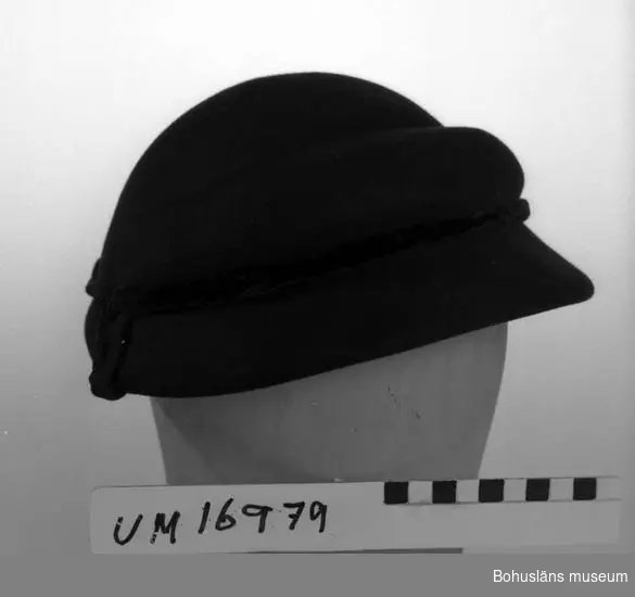 Svart formpressad hatt. Prydd med svart sammeband. 
Isydd band med text: "Modeaffär Ester Lundell Lysekil tel 319."