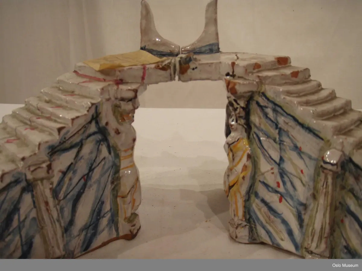 Scenografimodell av keramikk. Glasert i hvit bunnfarge med dekor/detaljer i blått og gult. 7 deler. Spesiallaget oppbevaringseske.