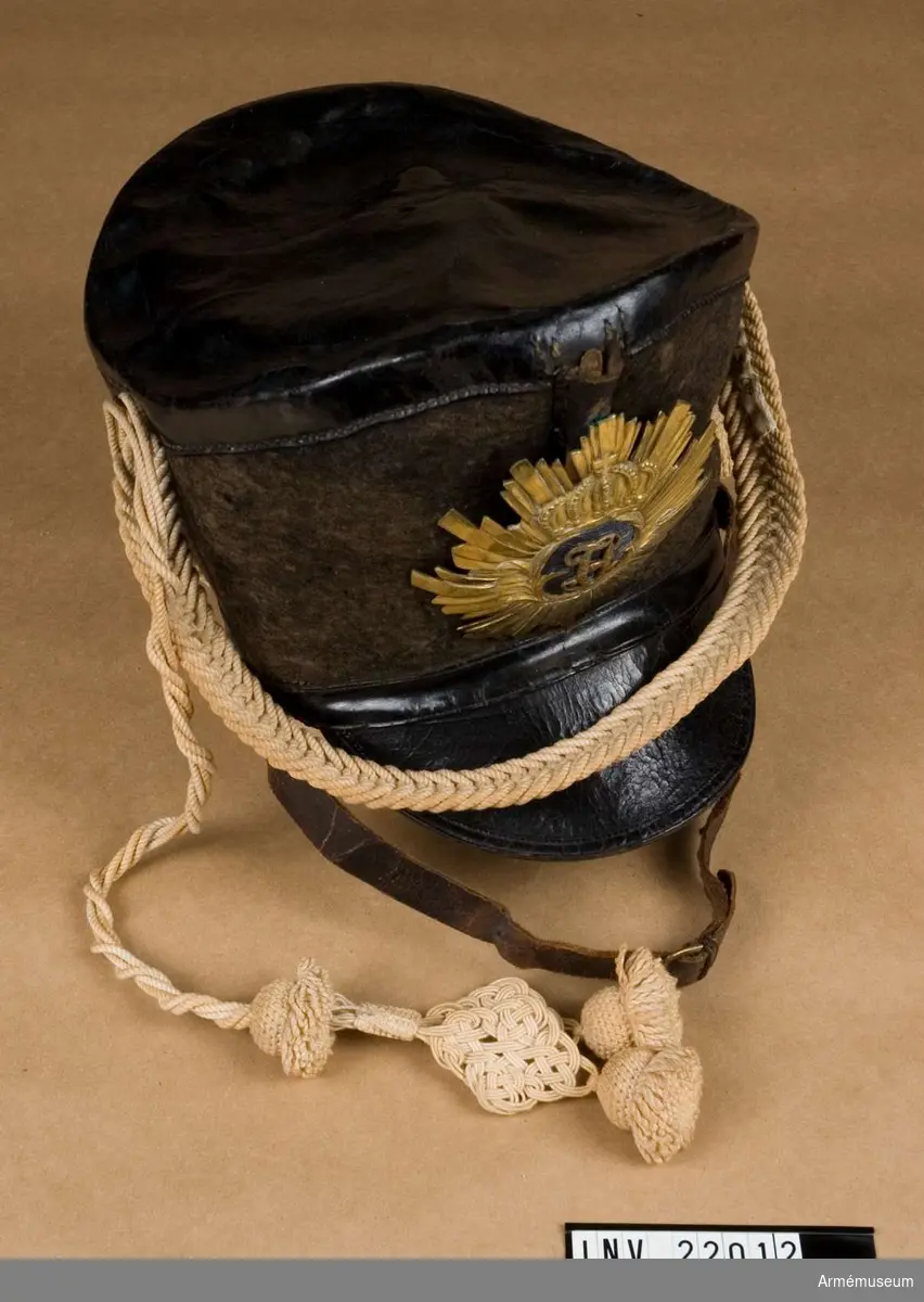 Grupp C I.
Tschakå av svart hattfilt med skärm av svart läder och vapenplåt med Karl XIV Johans namnchiffer.
