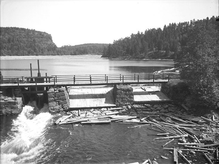 Enligt noteringar: "Dammbron i sjön Vassbotten vid Kaserna. Dammen reglerar vattenflödet till Munkedals bruk och var fram till år 1966 flottled för massaved till bruket. Innanför bommen, mitt i sjön, ligger timmer som flottats genom strömmarna från Viksjön i Dalsland."
(BJ)