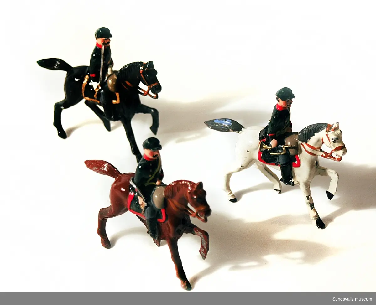 SuM 2765:1-8, tennsoldater i blå uniformer. En är trumslagare, fyra stycken bär gevär och tre sitter till häst, en vit, en brun och en svart. originalkartong i papp med tryckt text.