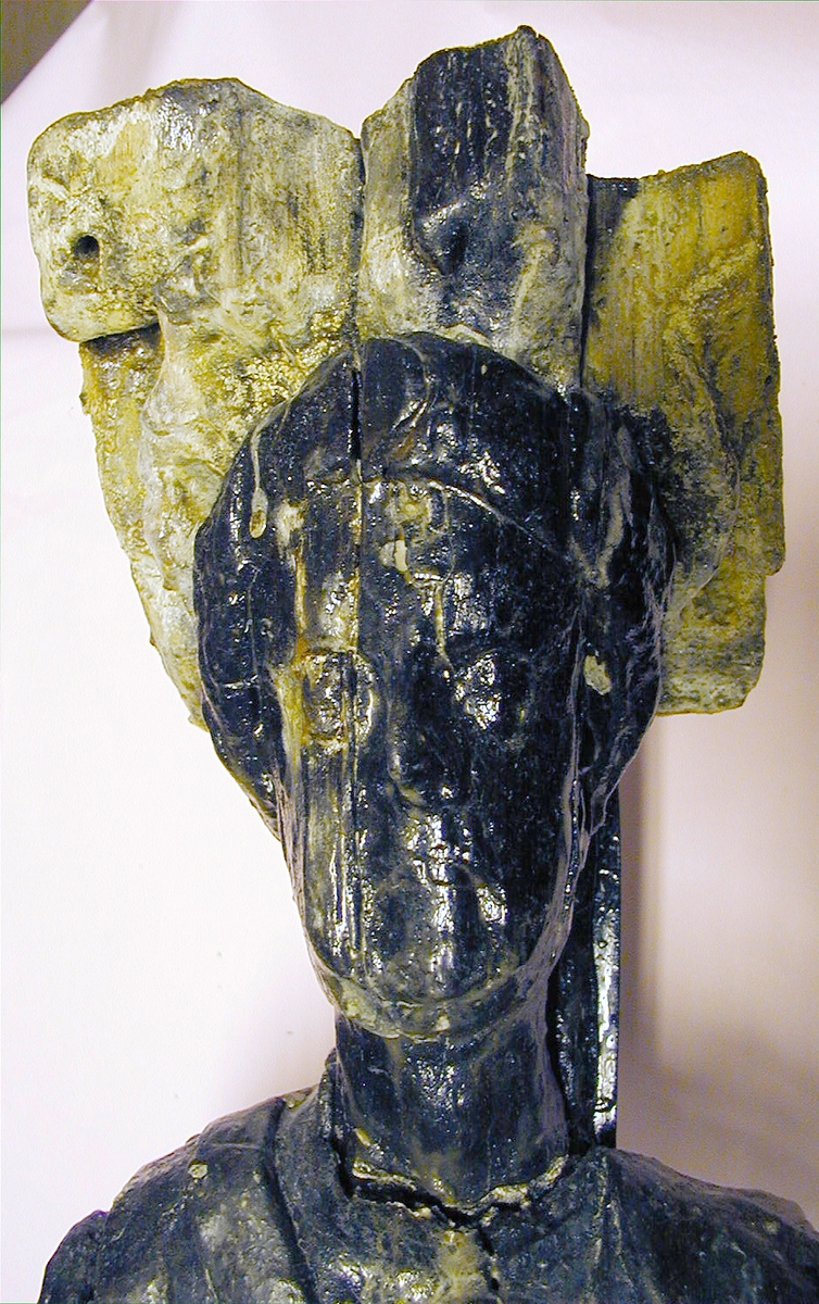 Skulptur föreställande en mansfigur iförd thoraxrustning med mantel. Huvudet är lagerkrönt och avtecknar sig mot ett stort snäckskal. Ansiktet är slätrakat.

Figurens huvud och kropp är riktade frontalt, en aning vridna mot vänster. Kroppstyngden vilar på vänster ben. Höger ben hålls böjt, med foten stödjande mot underlaget endast med tåspetsarna.

Figuren står på en sockel, vilken pryds av en maskaron. Upptill är bakstycket framdraget i en "huvudplatta" med kvartcirkelformad profil. Baksidan uppvisar tre snedställda, olika djupt liggande fält. De tre fälten, som utgör anliggningsytor, ger skulpturen en trappstegsformad profil.
Skulpturen är kraftigt sliten, framförallt huvudplattans framsida samt sockeln med maskaronen. Ursprungligen har sockeln varit prydd med en namninskription som dock är utplånad. Av manteln återstår endast en utefter vänster sida nedhängande del. Figurens hela högra arm med vidhängande del av mantel var bortbruten, liksom vänster underarm. Del av höger arm är funnen separat, och har monterats på skulpturen.

Text in English: Sculpture representing a male figure wearing thorax armour with mantle. The figure has a laurel-wreathed head and a clean-shaven face, backed by a large sea shell. The figure''s head and body face forward or are inclined slightly to the left. The body rests on the left leg, the right is bent and rests on its toes.

The figure stands on a plinth which bears a mask. The upper part of the back extends upwards in a "head board". The back has three obliquely placed flat surfaces of different depths, that are areas of attachment. The flat surfaces make the sculpture looks like a step-ladder in profile.
The sculpture is badly worn, especially the front of the board over the head and the plinth with the mask. The plinth has originally been decorated with a label bearing the name of the figure but no letters remain. The left side of the mantle have survived but that on the right side of the figure is missing. The left forearm and the whole of the right arm were also missing. Part of the right arm has been found separately and has been put together with the rest of the sculpture.