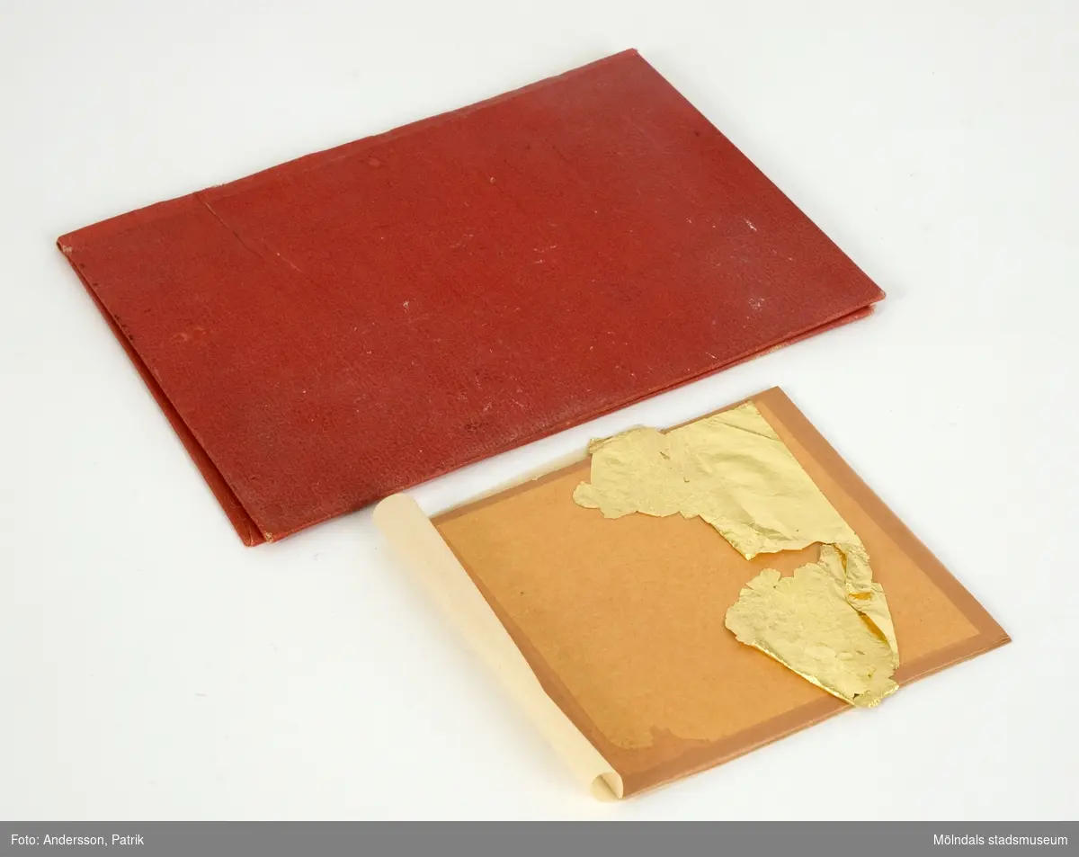 Bladguld i silkespapper, förvaras i pappfodral. 1: Röd pappärm (160x117 mm), textilklädd. Innehåller två små silkespappershäften, vari bladguldet ligger.2: Naturvitt papperkuvert (105x180 mm), som innehåller två små silkespappershäften, vari bladguldet ligger.3: De ovannämnda föremålen förvaras i ett avlångt, brunt kuvert, märkt "Bladguld" med blyerts. Kuvertet är mycket skört. 