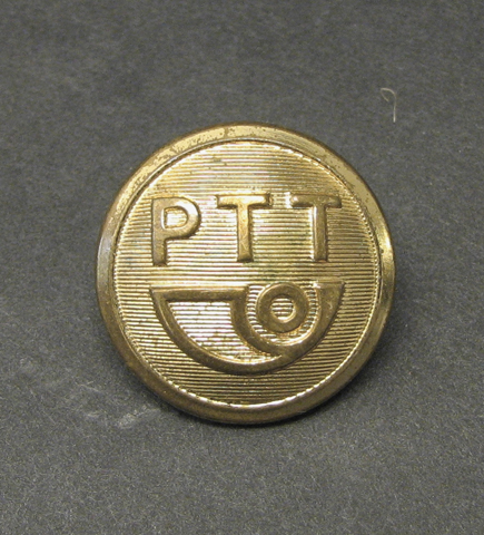 Knapp till uniform för brevbärare i Holland. På en
räffladbotten står bokstäverna PTT över en stiliserad postsymbol.
Knappen är bottnad och är dekorerad med slingor.
