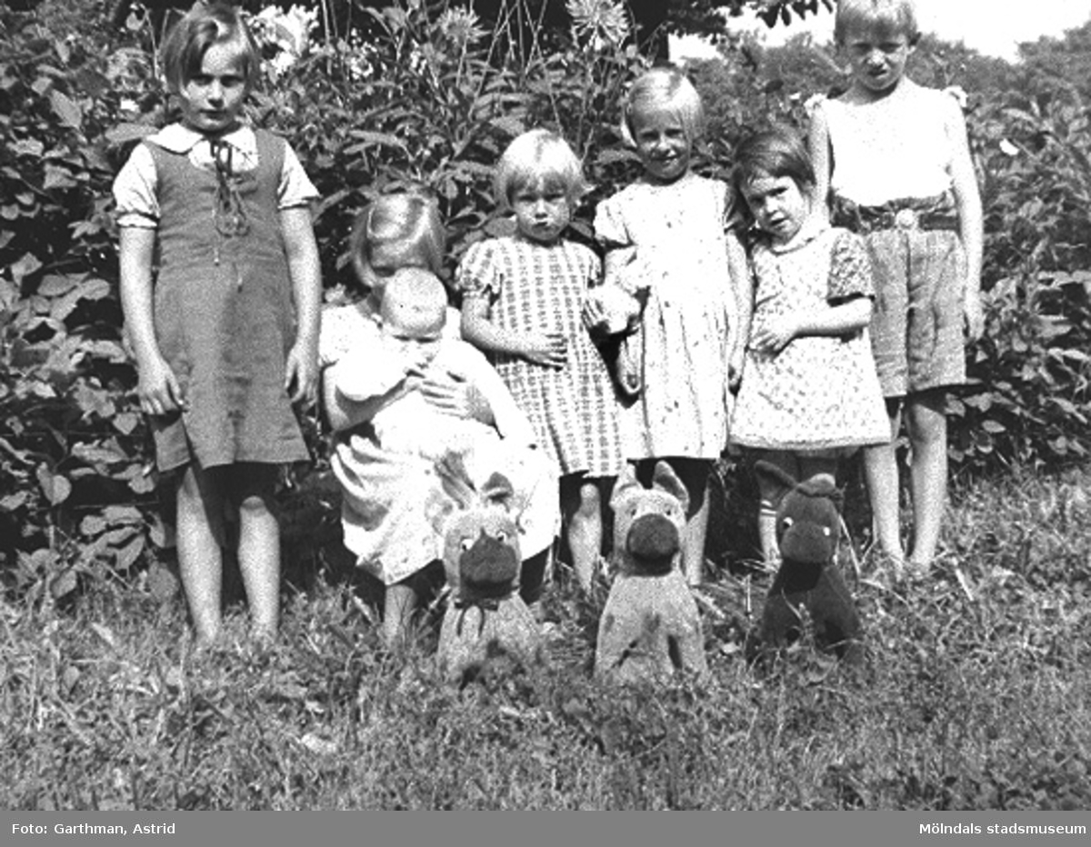 Barn boende vid Kvarnfallet 31, 1930. De står på en grässluttning framför några träd. Det är bland annat givarens mostrar och fastrar samt grannar till dem.