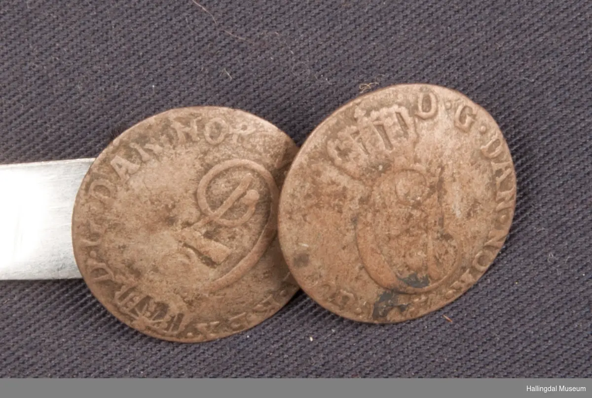 2 mynter, 2-skillingsmynter fra 1782 og 1784.  Forbundet med kringleformet sølvhempe som holder dem sammen i hempene.