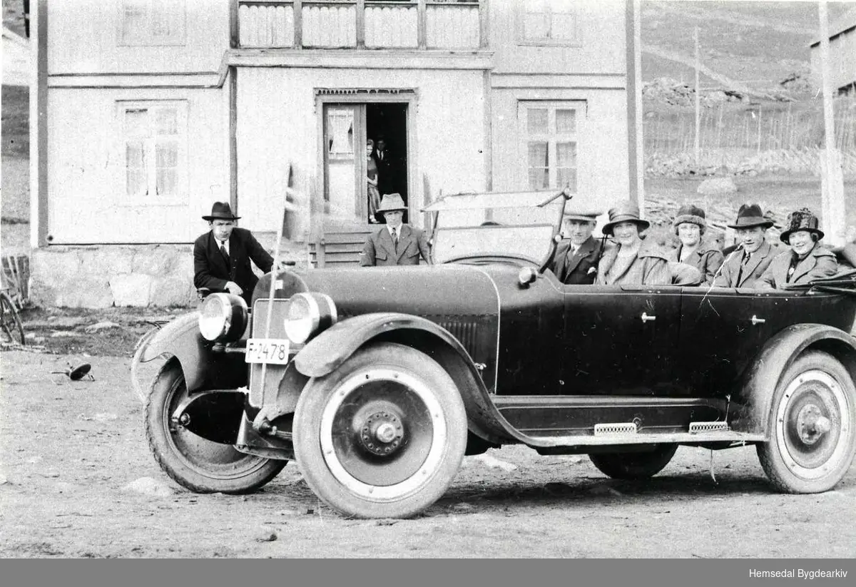 Frå venstre: Jon Hjelmen, Halvor K. Mythe, båe frå Hemsedal,  og sjåfør Knut Granheim frå Gol. Dei andre er ukjende. Bilen er ein 1923 Buick.