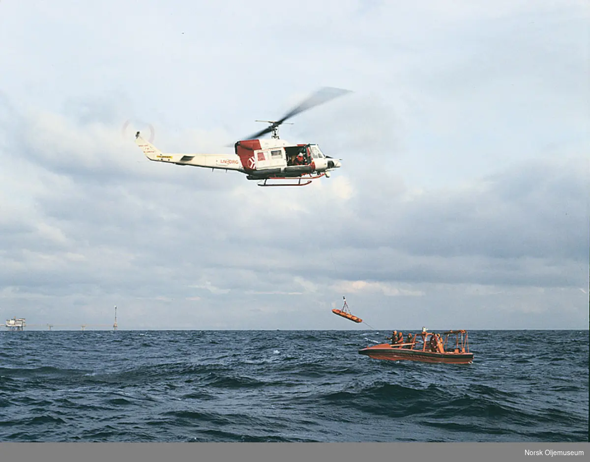Redningsøvelse på Ekofisk. En båre heises opp fra redningsbåt til helikopter. I bakgrunnen ses et flammetårn.