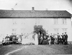 Gruppebilde av brudepar og slektninger, fotografert foran et