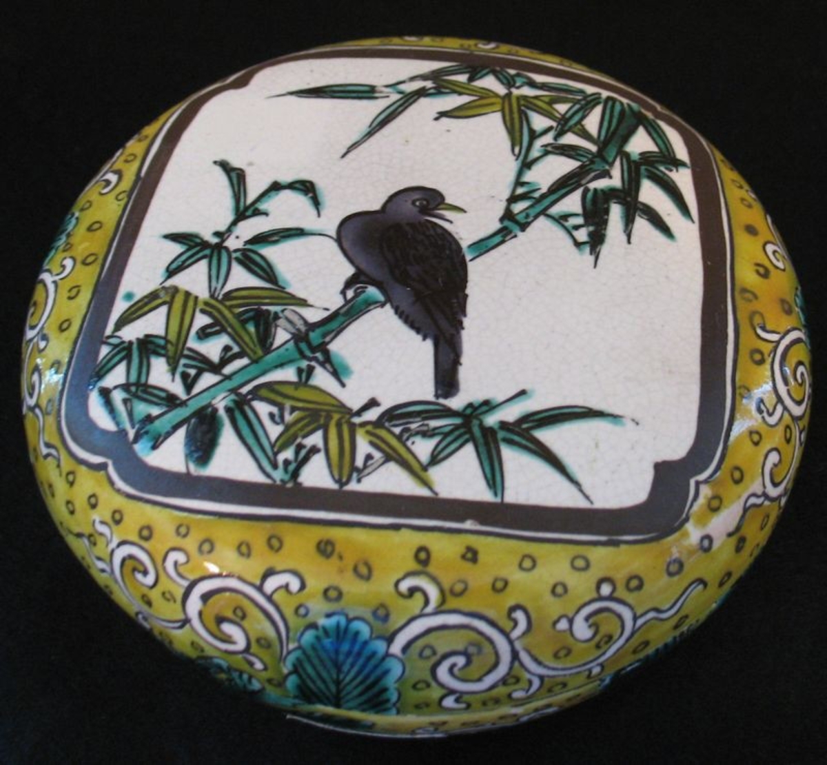Platt lock, dekor: fågel i bambuträd målad med gult, grönt, brunt och blått, på beigeaktig glasyr. Något krackelerad, omärkt.