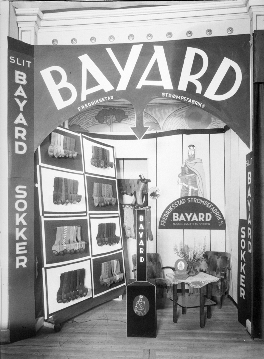 Reklame for Bayard Fredriksstad Strømpefabrik A/S. Utstilling med sokker og reklameskilt med ridder. Fra handelsmesse.