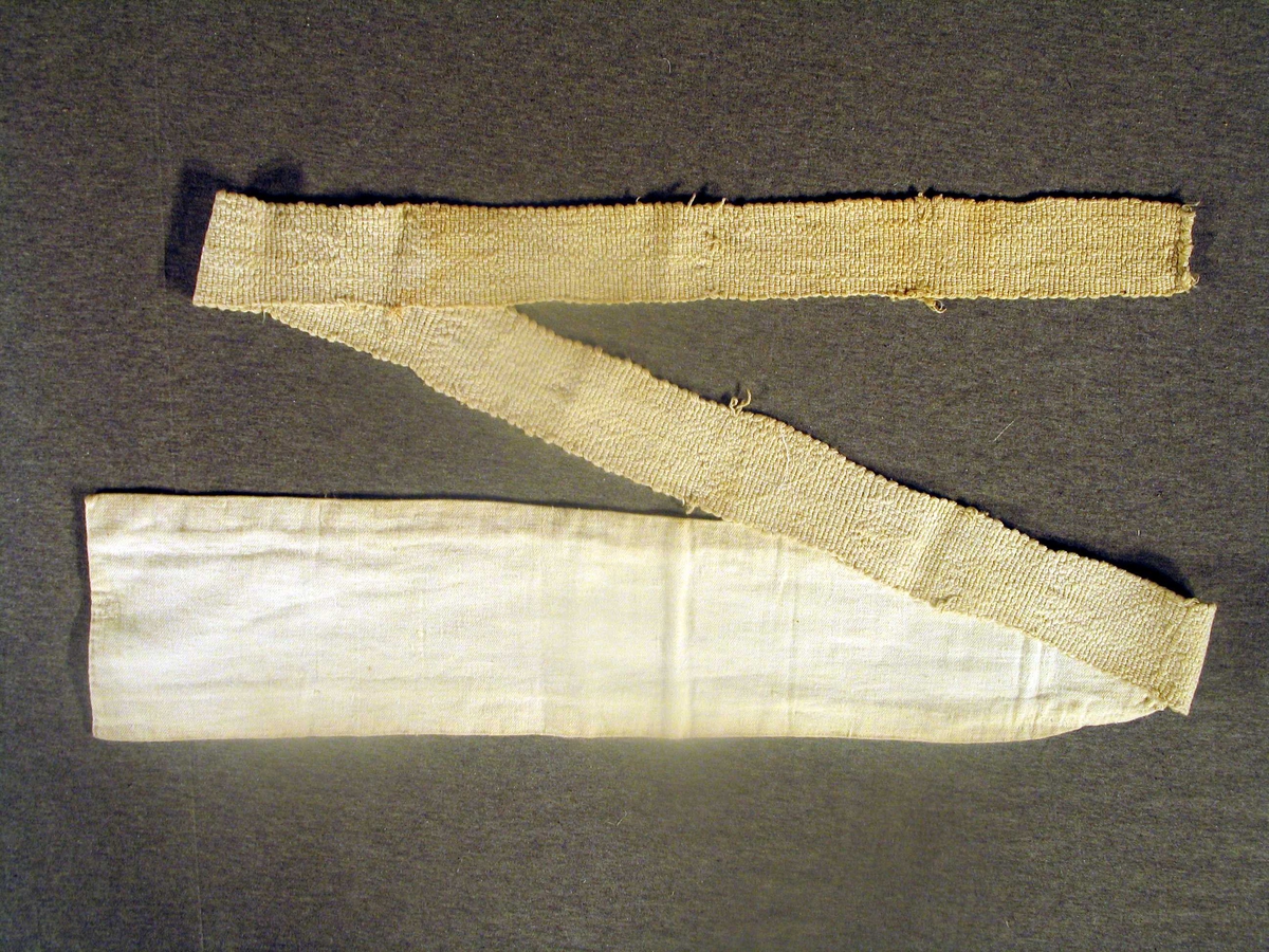 Breitt band av twill, fora med flanell. Smalnar av i eine enden og festa til eit breitt vove juteband.
Tilvekstprotokoll/kortkatalog kring. 1955:
"Linne. Tvill og vove band."
Til bruk utanpå reiveplagga ved reiving av spedbarn.