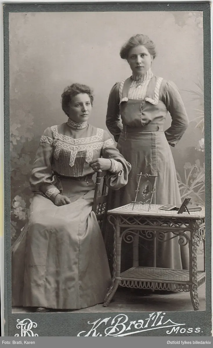 Visittkort av to venninner, i tidsrommet ca. 1906-1909.
Damen til høyre er Helga Syverød F. 1886 D.1949. 
Gift med Julius Mellegaard, som drev gården Mellegård i Våler. Flytta til Varteig i 1928.