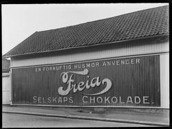 Gateparti, reklameskilt, Freia Selskapssjokolade, 
Tekst: E