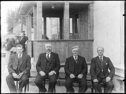 Gruppe menn sittende på en benk utendørs.