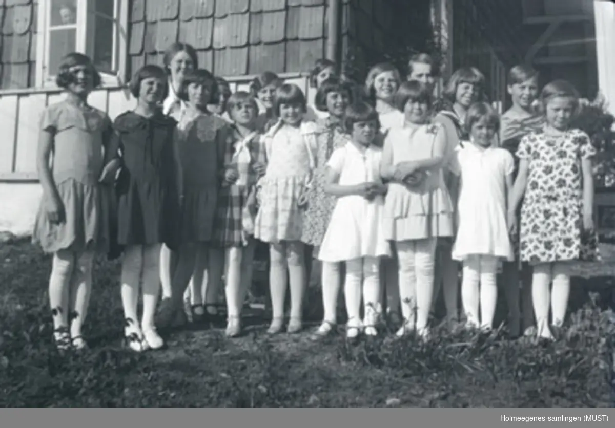 Atten jenter i kjole og knestrømper foran huset på Holmeegenes i Stavanger.