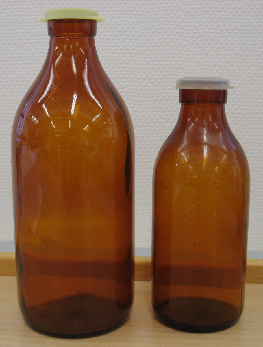 Två bruna flasflaskor med plastkapsyler i två olika storlekar, 1 liter och 1/2 liter. Glasflaskorna användes vid inköp av mjölk på söndagar. Då gick man, ofta ett barngöra, givaren gjorde det ofta som barn, till affären och fyllde på mjölk i dessa förutbestämda mått. 1liter och 1/2 liter var till mjölk. Före dessa glasflaskor var det aluminiumflaskor som man använde.