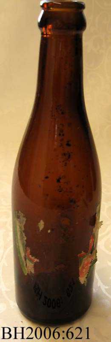 Ølflaske av brunt glass med  etikett av papir på flaskens front. 