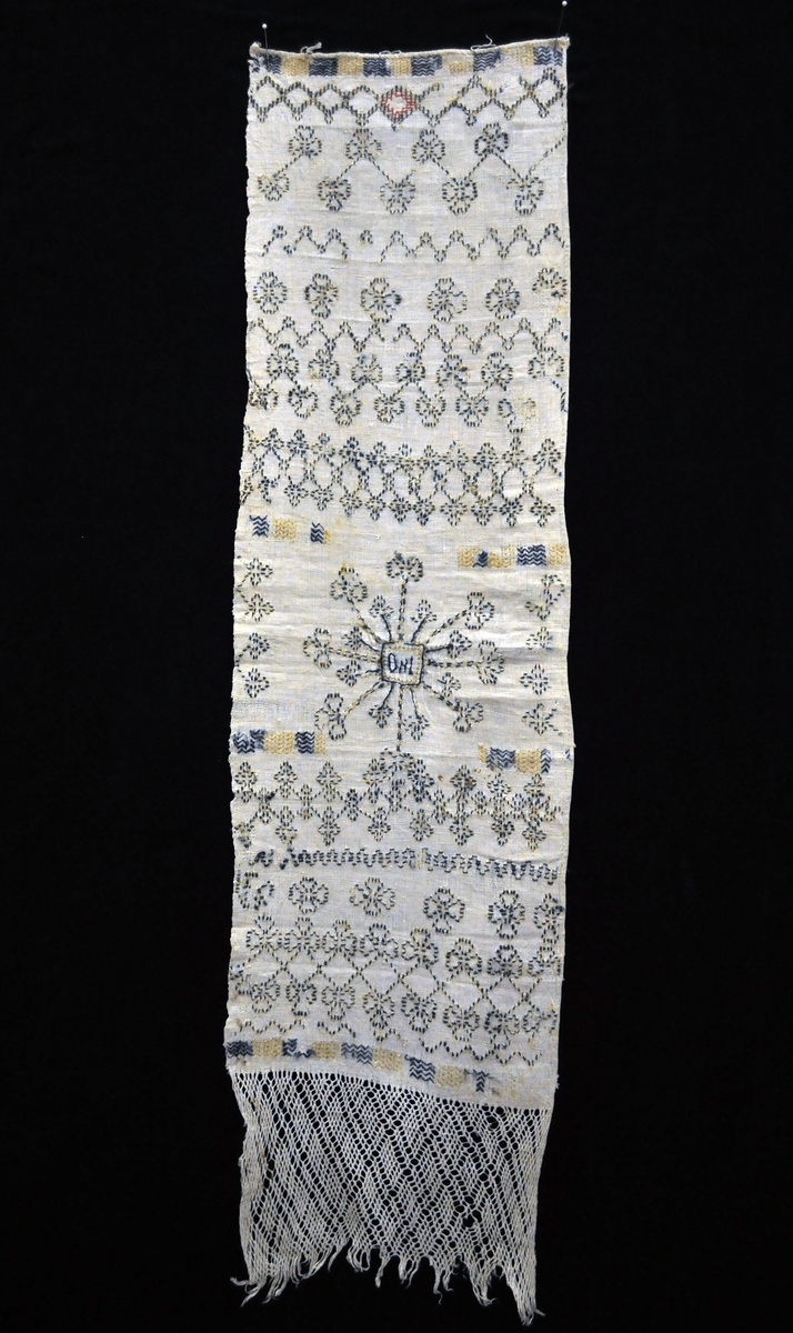 Fra protokollen: Handklæde i blaa og gul krunesaum. I enden knipling av sprang.
(= firfletting).