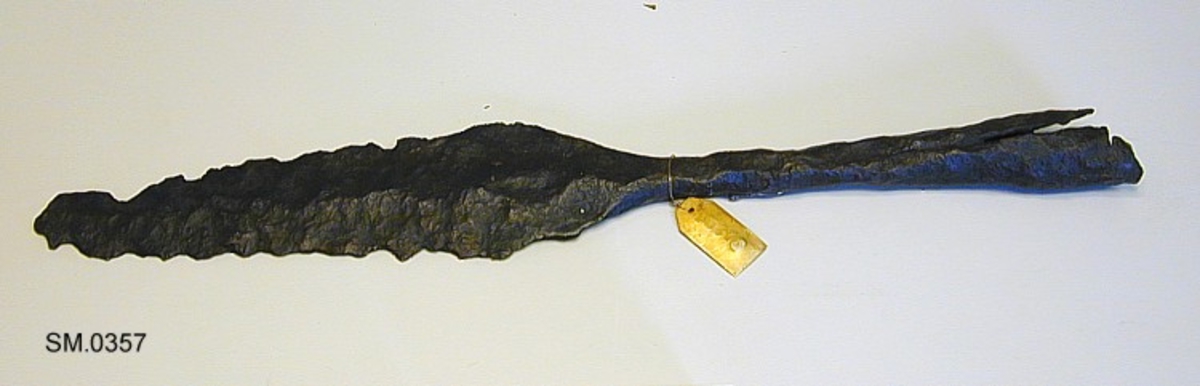 Ujevnt fasettert fal, skrå, jevn overgang til bladet, som er rygget og som det synes med jevne egglinjer - disse er nå rustet bort og odden mangler.
Vikingtids gravfunn - spydspiss av jern, som Jan Petersen: Vikingesverd fig. 35 el. Rygh 529, 30, 32.