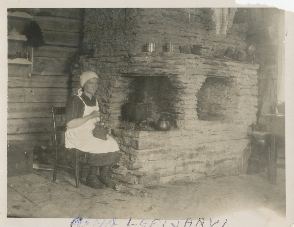 En kvinne sitter ved peisen i sitt hjem og kverner kaffe.