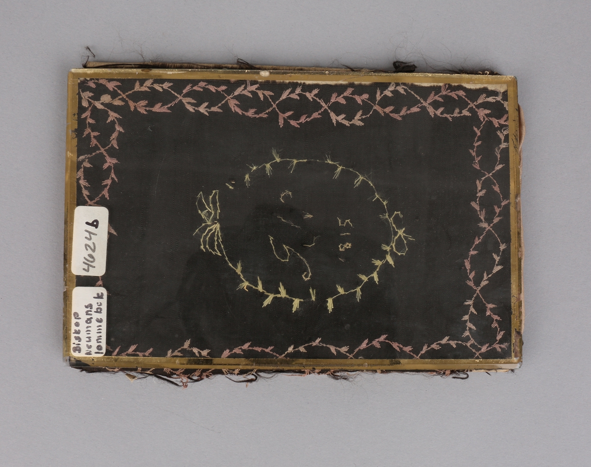 Rektangulær lommebok av papp trukket med silkerips. Fóret med silke. Broderte bladranker og monogram.