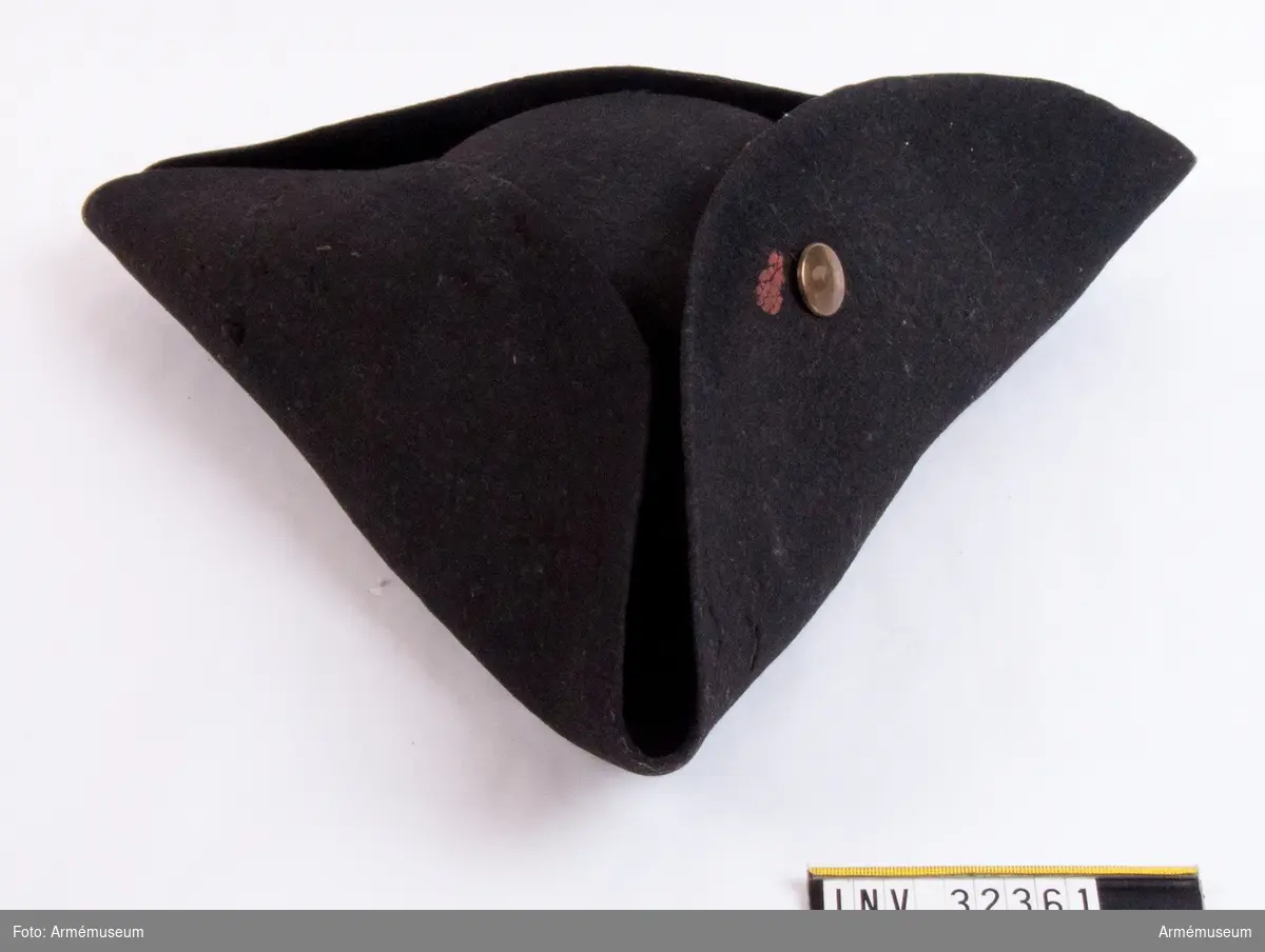 Trekantig svart hatt med mässingsknapp och rester av rött lacksigill.