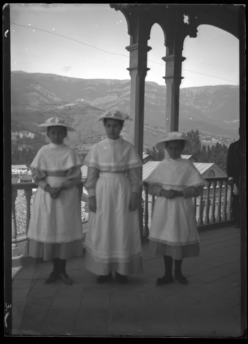 '3 barn (flickor) ståend epå balkong med träräcker, med utblikc över stad i bakgrunden. Berg i fonden. ::  :: Ingår i serie med fotonr. 5280:1-17. Se även fotonr. 5269-5292 med bilder från Stuxbergs resa till Kaukasien.'