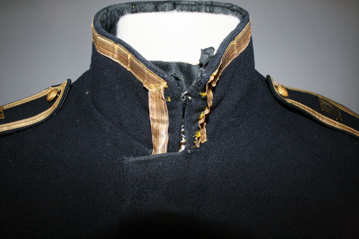 Uniformsjakke i sort med blåskjær med gulfknapping over seks knapper. To brystlommer med klaff. Stående krage kantet med 12 mm gullbånd. Skulderklaffen har et 7 mm gullbånd med en løveknapp og metallnummer romertall 2.