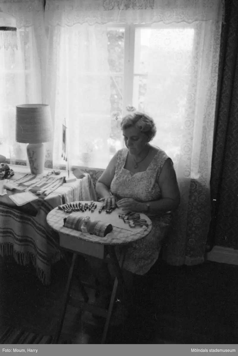 Lindome Hembygdsgille firar 20-årsjubileum på Börjesgården i Hällesåker den 23 juli år 1983. En kvinna knypplar.

För mer information om bilden se under tilläggsinformation.
