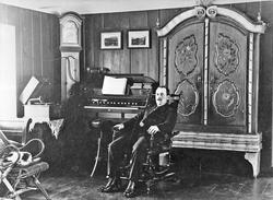 Mann i stol. Golvur. Skap. Orgel.