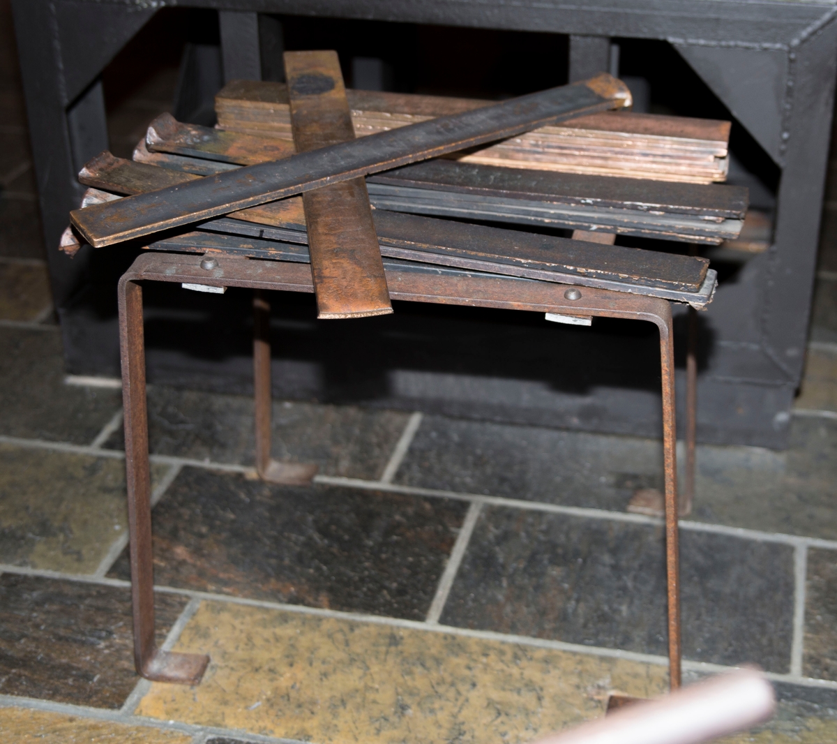 Flate jernplater montert sammen med stålnagler slik at de danner ett stativ med flat topp og fire bein. 15 teiner er montert på stativet.