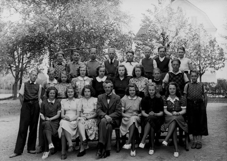 Almby skola, 12 flickor, 12 pojkar och lärare Albert Johansson på skolgården.
Klass 7.
Skolbyggnad i bakgrunden.
