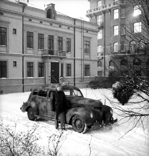 Fo-staben, bilarna. Bilen är en Dodge 1939. En man vid bilen. 
Byggnaden i bakgrunden har adress Olaigatan 21/Slottsgatan 2. Till höger på bilden Centralpalatset.
