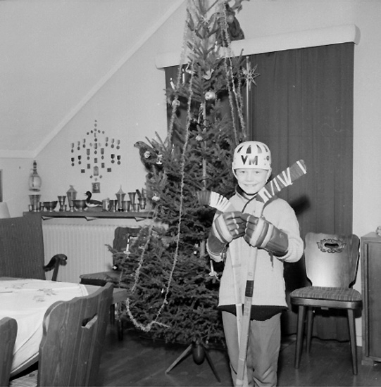 Rumsinteriör, en pojke i ishockeydräkt vid julgranen.
Hasse
