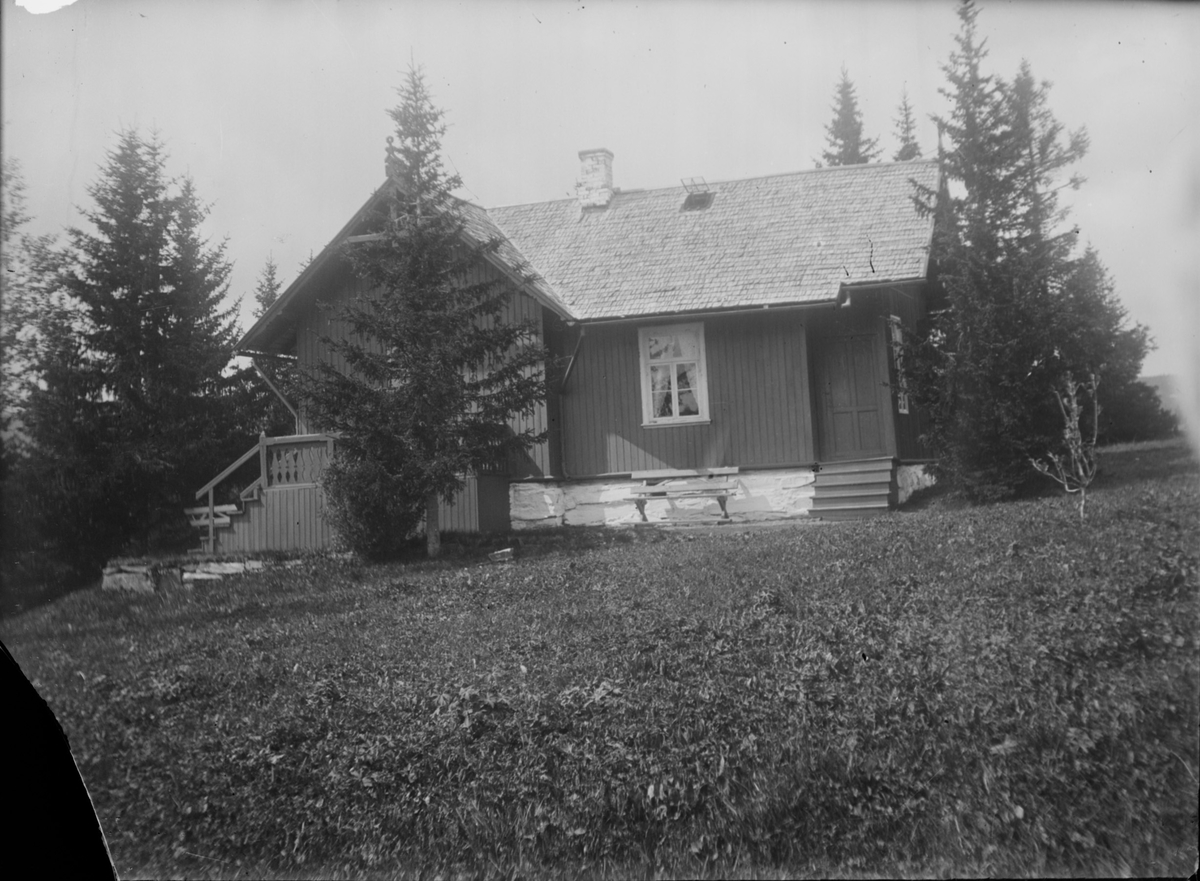 Et lite hus står i et landskap med gressbakker som er slått og spredte grantrær.