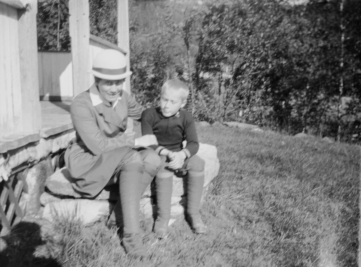 Celina Ihlen Mathiesen sitter på en steintrapp, utenfor en fritidsbolig i Jeppedalen, sammen med en av sønnene.
