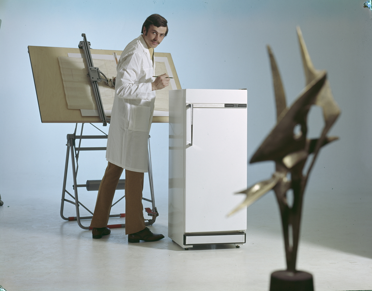 Reklamefoto for kjøleskap. En mannlig modell er utkledt som ingeniør foran tegnebordet. ..