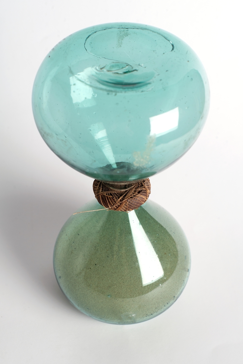 Timglas hopsatt av två flaskor av ljusgrönt glas innehållande vit sand. Flaskorna är surrade med linnetråd i hopsättningen.