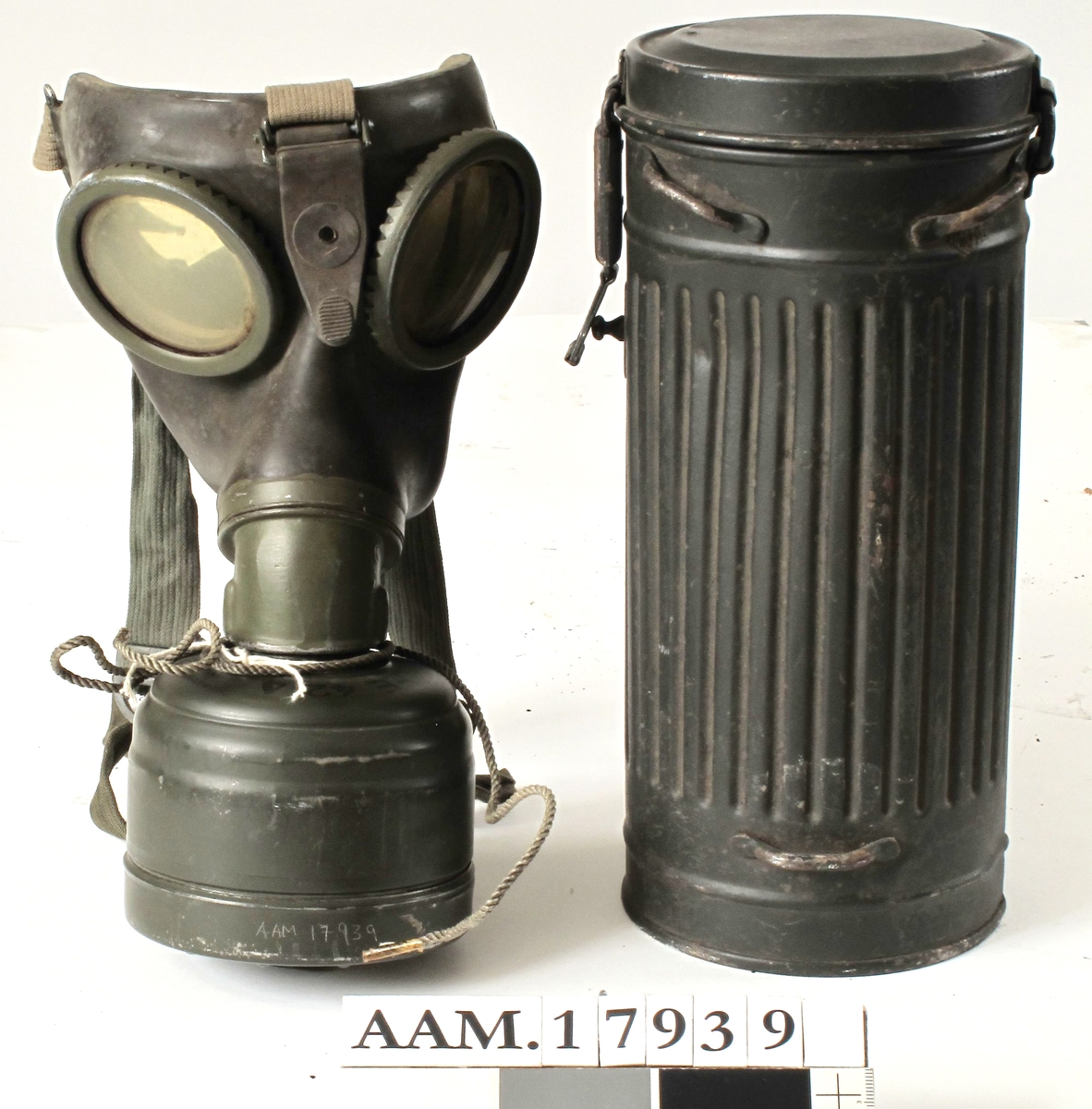 Gassmaske, tysk, fra krigen 1940-45. Sylinder av   jernblikk,  malt  mørk grønngrå.  
Rifllet beholder med flatt lokk, i bunnen  ligger gassmasken, over denne en beholder,  malt med sort : byd Fe, Fe 424, tyske våpen og WA. A.533.