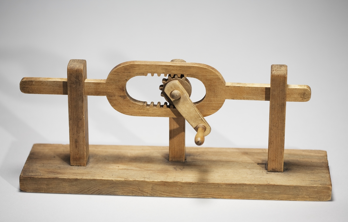 Modell ur Polhems mekaniska alfabet. Text på föremålet: "XV". En roterande rörelse hos hjulet, som till hälften är försett med kuggar, överförs till en fram- och återgående rörelse hos den bygelförsedda armen.